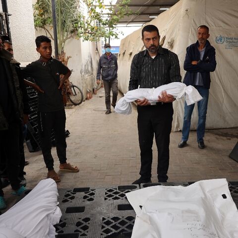 Outside the morgue of a hospital in Rafah, the southern Gaza Strip, a man carries the shrouded body of a child killed in Israeli bombardment